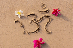 Om symbol drawn in the sand surrounded by tropical flowers, representing spirituality, meditation, and mindfulness.