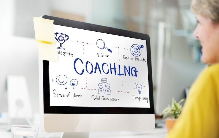 Employee looking at computer screen displaying key coaching traits: integrity, vision, positive attitude, sense of humor, solid communicator, inspiring