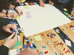 People engaged in a group activity using LEGO bricks and sticky notes, representing team collaboration, gamified learning, and creative workshop practices like Lego Serious Play."