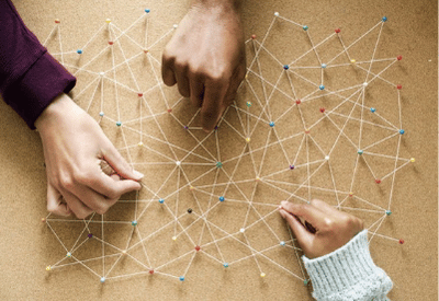 Teamwork concept showing hands connecting threads across colorful pins on a board, symbolizing collaboration, networks, and systems thinking.